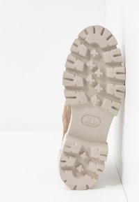 Semelle de botte beige avec un motif de bande de roulement profond et robuste conçu pour l’adhérence, une marque visible et un matériau en caoutchouc clair.