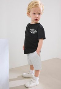 Svart kortärmad skjorta med tryck av "ATHLETIC STATE", ihop med grå shorts och vita sneakers. Subtila texturer, avslappnad passform.