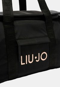 Borsone in nylon nero con logo a contrasto in oro rosa. Presenta manici robusti e una tasca frontale con chiusura a zip.
