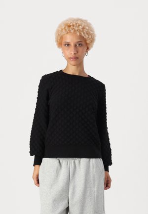 Black textured sweatshirt featuring a quilted pattern, round neckline, and long sleeves, paired with light gray sweatpants.