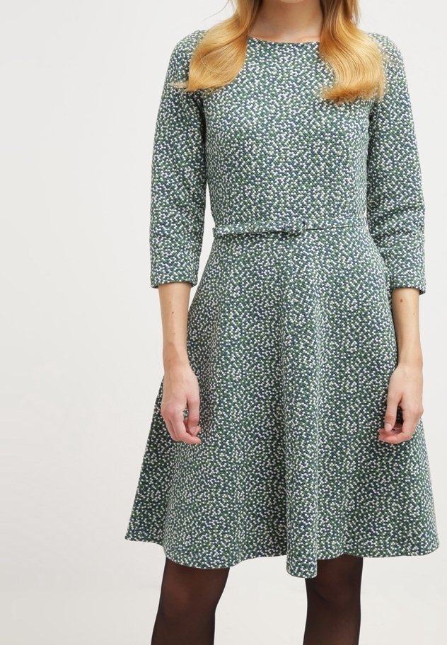 Vihreä kuvioitu mekko, jossa on kolmen neljänneksen hihat, korostettu vyötärö ja liehuva hame; siinä on pieniä valkoisia ja sinisiä kukkakuvioita.