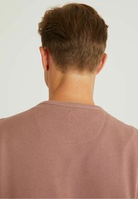 Suéter en un suave color rosa apagado con un cuello acanalado. Presenta un sutil detalle bordado en la parte posterior con un hilo en contraste.