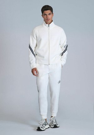 White zip-up athletic jacket with black stripe accents, paired with matching white joggers featuring side stripes and a logo detail.