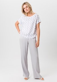 Lichte, korte mouw top in het wit met een geometrisch patroon; gecombineerd met lichtgrijze, wijde broek in een gladde stof.