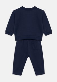Marineblå todler to-dels sett med langermet topp og bukser med elastisk midje, med en baklomme, vist flatt bakfra.