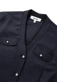 Camisa de botón en un azul marino oscuro con cuello en V, dos bolsillos frontales y botones de presión plateados, con un acabado de tela suave y duradera.
