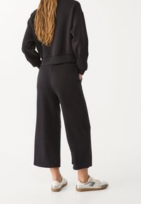 Schwarzes Sweatshirt und weit geschnittene Hose aus weichem Stoff. Mit verkürzter Länge, lockerer Passform und seitlichen Taschen. Sneakers mit silbernen Akzenten.