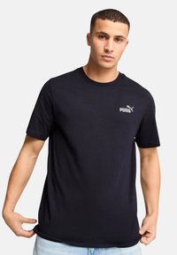 Zwart katoenen t-shirt met korte mouwen en ronde hals, voorzien van een klein zilveren Puma-logo op de linker borst. Zachte structuur, rechtvallende pasvorm.