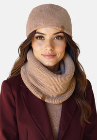 Strikket beige hue med foldet brem, parret med et matchende ribbet infinity-sjal. Begge har en subtil tekstur og et mærke.