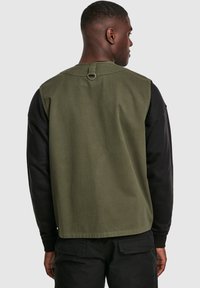 Oliwkowa bluzka z krótkim rękawem z czarnymi rękawami. Ma detal w postaci pętli na plecach, prosty krój i gładką teksturę materiału.