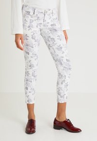 Vita jeans med blommönster i ljusgrå blommor, medelhög midja, smal passform och framfickor med dragkedja. Matchas med blanka röda snörskor.