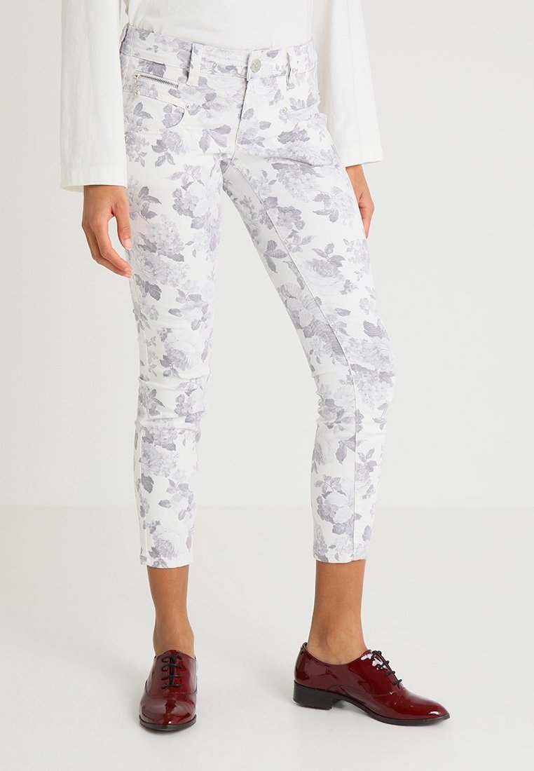 Vita jeans med blommönster i ljusgrå blommor, medelhög midja, smal passform och framfickor med dragkedja. Matchas med blanka röda snörskor.