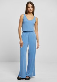 Blå jumpsuit med rund hals og justerbar snor i taljen. Lavet af blødt stof, den har brede ben og en glat tekstur.
