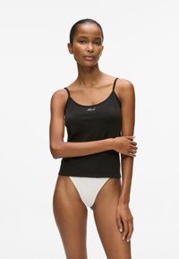 Melna kokvilnas topiņš ar plānām siksnām, uz kura priekšpusē ir logo. Kombinēts ar gaišas krāsas zemu jostasvietu g-string. Gluda tekstūra.