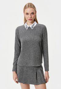 Maglione grigio a maglia con colletto bianco decorato con applicazioni floreali, maniche lunghe e vestibilità dritta. Abbinato a una gonna plissettata coordinata.