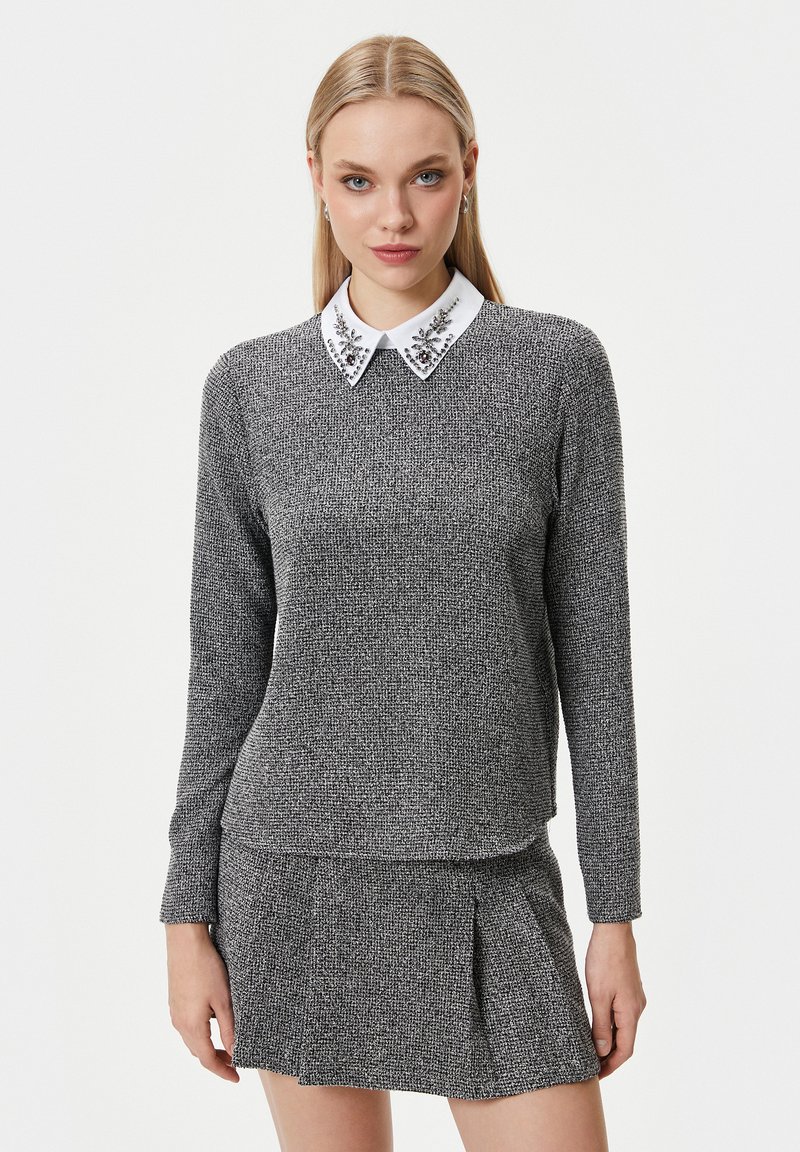 Maglione grigio a maglia con colletto bianco decorato con applicazioni floreali, maniche lunghe e vestibilità dritta. Abbinato a una gonna plissettata coordinata.
