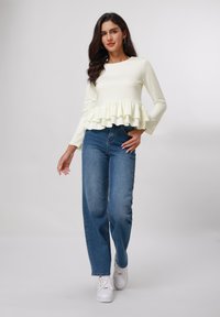 Top blanco de manga larga con un dobladillo con volantes, combinado con jeans azul de cintura alta y zapatillas blancas. Diseño simple y casual.