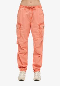 Perzikkleurige cargobroeken met een drawstring taille, twee zijzakken en elastische boorden. Gemaakt van lichte stof met een comfortabele pasvorm.