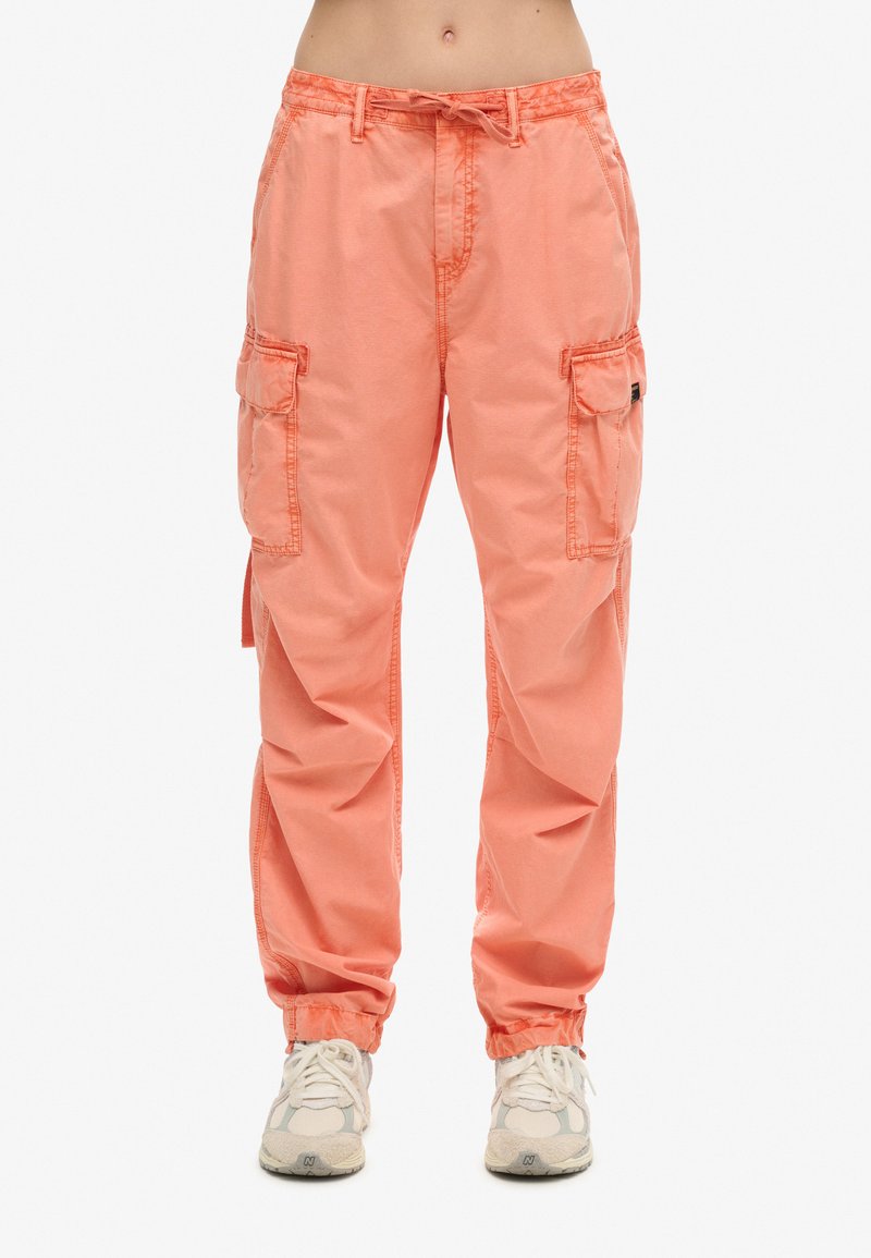 Perzikkleurige cargobroeken met een drawstring taille, twee zijzakken en elastische boorden. Gemaakt van lichte stof met een comfortabele pasvorm.