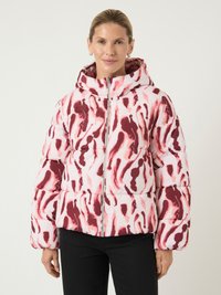 Mulher vestindo uma jaqueta puffer com capuz em padr�ões abstratos rosa e vermelho, com fecho frontal, combinada com calças pretas.