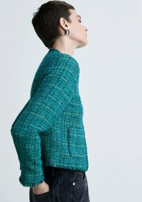 Giacca teal con texture e motivo a tessitura, di lunghezza cropped e maniche lunghe. Presenta tasche laterali e polsini sfilacciati.