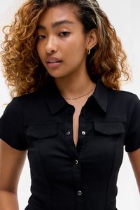 Svart skjorte med korte ermer, med to brystlommer, sølvfargede trykknapper og en tettsittende design. Glatt stoffstruktur.