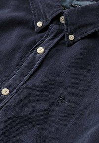 Navyblauwe corduroy overhemdbloes met witte knopen en een klein geborduurd logo op de borst.