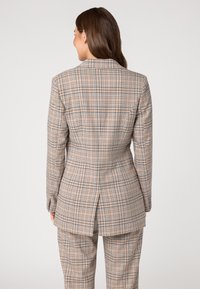 Proužkovaný béžový blazer s modrými akcenty, má rozparek na zadní straně, dobře padnoucí střih a dlouhé rukávy, kombinovaný s odpovídajícími kalhotami.