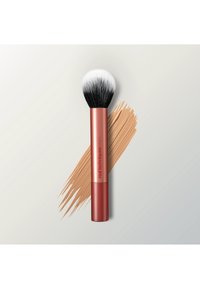 Make-upkwast met zwarte en witte haren en een rood handvat met het label "real techniques", geplaatst over een beige foundationstreep op een lichte achtergrond.