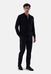 Marinefarbener Strick-Button-Up-Hemd mit einem strukturierten Rautenmuster, kombiniert mit maßgeschneiderten dunklen Hosen und schwarzen Slippern, was einen harmonischen Look schafft.