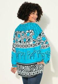 Blauw en witte blouse met een patroon van dierenafdrukken, sterren en de tekst "Happy." Losse fit met lange mouwen en een gebogen zoom.