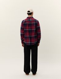 Rød og marineblå ternet flannel skjorte med lange ærmer, ryggen med yoke og rundet kant, parret med sorte bukser og en lys kasket.