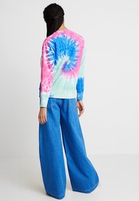 T-shirt med tie-dye i pastelfarver: pink, turkis og blå. Løs pasform, lange ærmer samt ribbede manchetter. Kombineret med brede denimbukser.