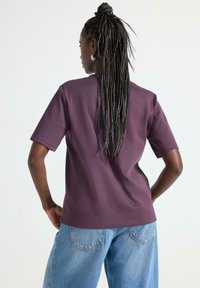 Lilla kortærmet t-shirt med en afslappet pasform, lavet af glat stof. Kombineret med lyseblå løse jeans for et afslappet look.