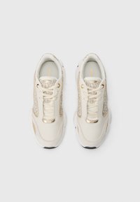 Sapatilhas bege com um cabedal em pele lisa, detalhes estampados, ferragens douradas e uma sola de borracha branca. Design clássico com atacadores.