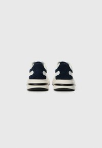Mørkeblå mokkasinsneakers med kremfargede detaljer, med en robust såle og utskjæring bak på hælen. Glatt tekstur og minimalistisk stil.