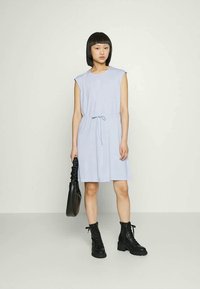 Vestido azul claro com mangas curtas e cintura ajustável, feito de tecido macio. Estilizado com botas pretas de atacadores e uma bolsa preta.