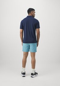 Camisa polo azul marino de manga corta, combinada con pantalones cortos azul claro. El conjunto se complementa con zapatillas negras y calcetines blancos.