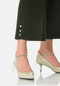 Gröna rutiga vida byxor med tre guldknappar vid fållen, kombinerade med ljusgröna läderklackar med kristallankelrem.