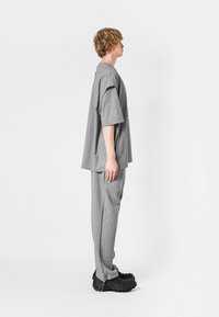 Camiseta gris de gran tamaño y pantalones de chándal a juego, hechos de una tela suave, con un corte relajado. El calzado es negro con una superficie texturizada.
