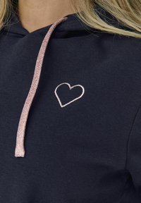 Felpa navy con tessuto testurizzato, un laccio metallico rosa e un piccolo design a cuore ricamato sul davanti.