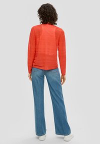Haut à manches longues texturé rouge avec des rayures horizontales associé à un pantalon en denim bleu taille haute et des baskets blanches.