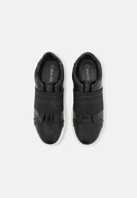 Baskets noires avec une tige en cuir lisse, bande élastique au milieu du pied et semelle en caoutchouc blanche. Logo présent sur la doublure intérieure.