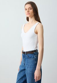 Canotta bianca a coste con scollatura a V, abbinata a jeans in denim blu a vita alta e una cintura marrone. Linea semplice e aderente.