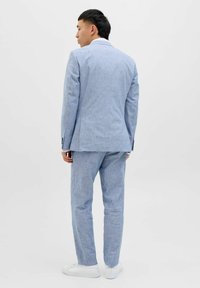 Costum albastru deschis dintr-un material texturat, cu sacou cu un singur rând de nasturi și pantaloni asortați. Adidași albi completează ținuta.