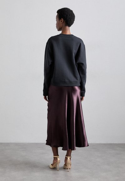 Μαύρη φούτερ, χαλαρή εφαρμογή, στρογγυλή λαιμόκοψη. Ρο flowing φούστα από σατέν σε σκούρο μπορντό, μήκους πάνω από τον αστράγαλο με γυαλάδα. Άσπρες ψηλές σαμπάνες με στοιχεία από διχτυωτό υλικό.