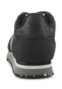 Sneaker nera con tomaia testurizzata simile alla pelle di serpente, dettagli in tessuto liscio e suola grigia maculata. Design minimalista e colori neutri.