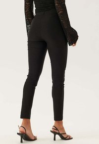 Zwarte skinny pants van rekbaar materiaal, met een hoge taille en een slank ontwerp, gecombineerd met zwarte sandalen met bandjes.