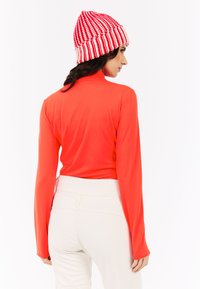 Rode lange mouwen top met een hoge hals, gecombineerd met lichtgekleurde high-waisted broeken. Een rode en witte gestreepte gebreide beanie maakt de look compleet.