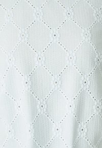 Bílá texturovaná tkanina s diamantovým vzorem malými výřezy, vytvářející jemný a vzdušný vzhled.